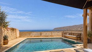 Ein rechteckiger Swimmingpool mit klarem, blauem Wasser, umgeben von einer Holzterrasse und einer Steinmauer.