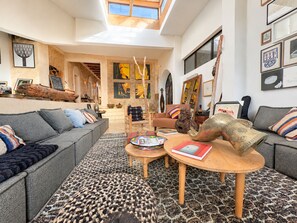 Amplia sala de estar con techo alto, un ventanal y vista al interior. Incluye un conjunto de sofás, una mesa de centro y un tapiz con diseño.