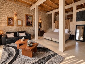 Una habitación amplia con una cama grande, un sofá y una mesa de centro. Hay cuadros enmarcados en la pared y un techo de madera.