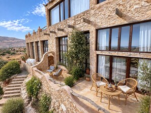 A stone building with large windows, outdoor seating, and a view of the landscape.