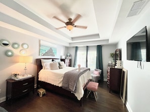 A bedroom with a bed, bedside tables, a ceiling fan, a TV, and a window with curtains. - Dream mansion located 20 minutes away from DTWN (Kennesaw)