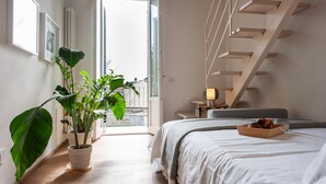 Ein Schlafzimmer mit einem Bett, einer Topfpflanze, einem Nachttisch, einer Lampe und einer Treppe.
