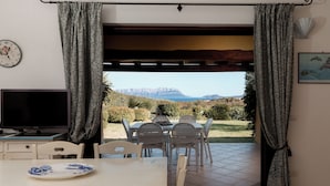 Quarto com mesa de jantar, cadeiras, televisão e cortinas.