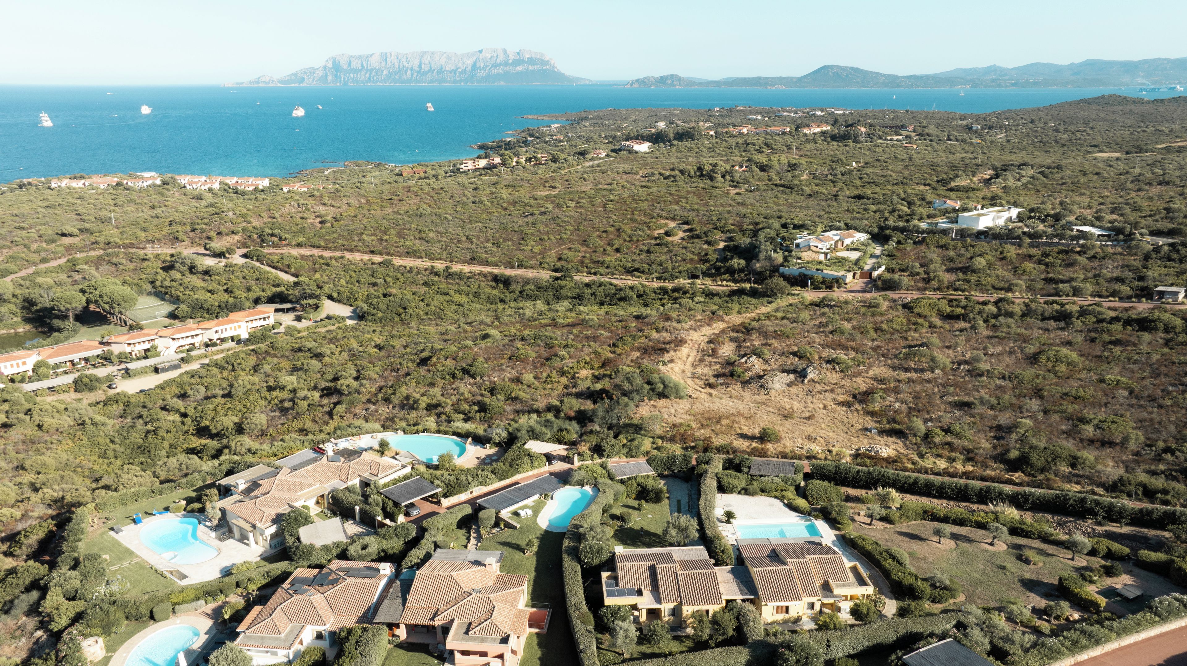 A coastal residential area with multiple houses, a swimming pool, and a view of the sea.