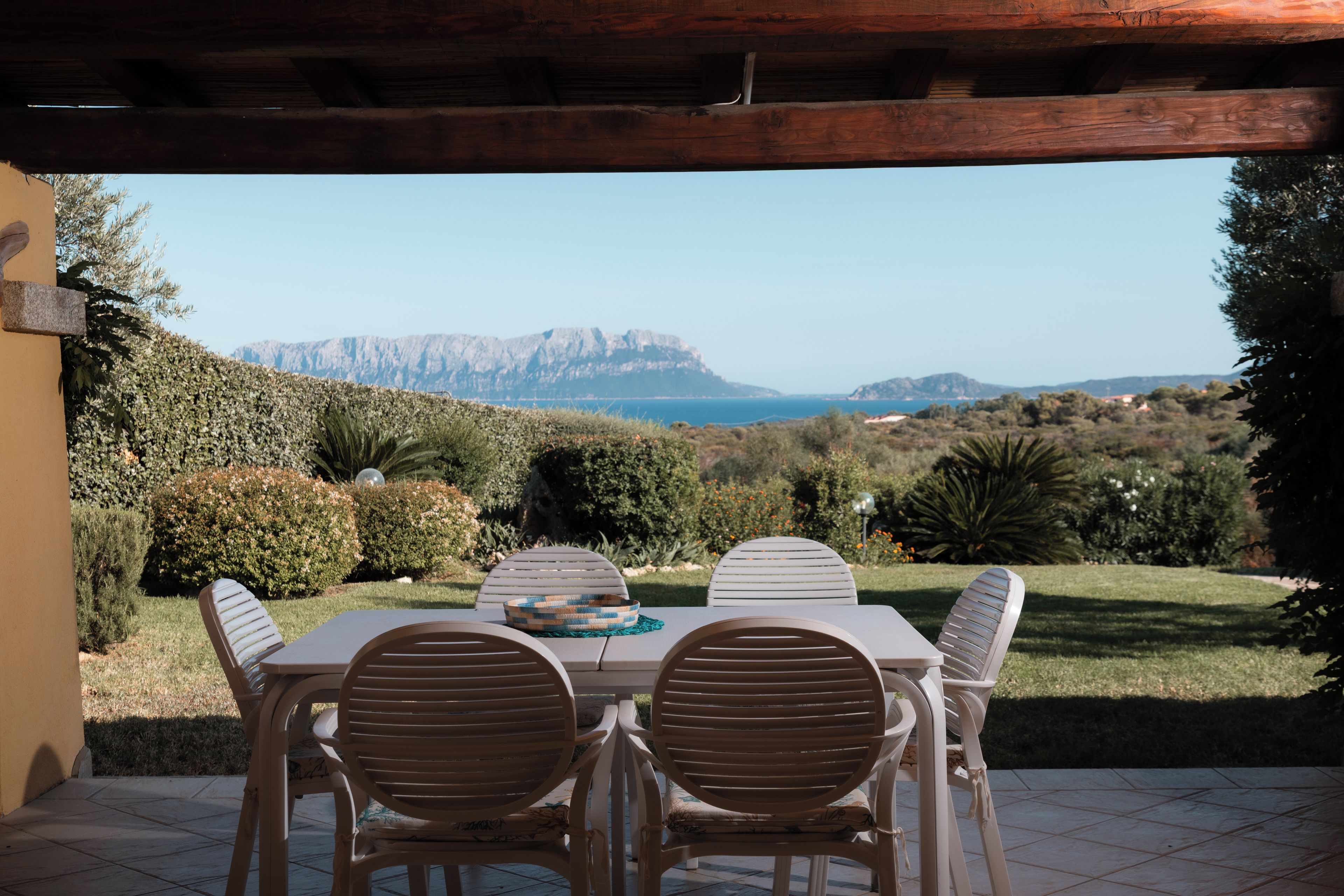 An outdoor patio with a table and chairs, overlooking a mountainous landscape and the sea.