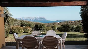 An outdoor patio with a table and chairs, overlooking a mountainous landscape and the sea.