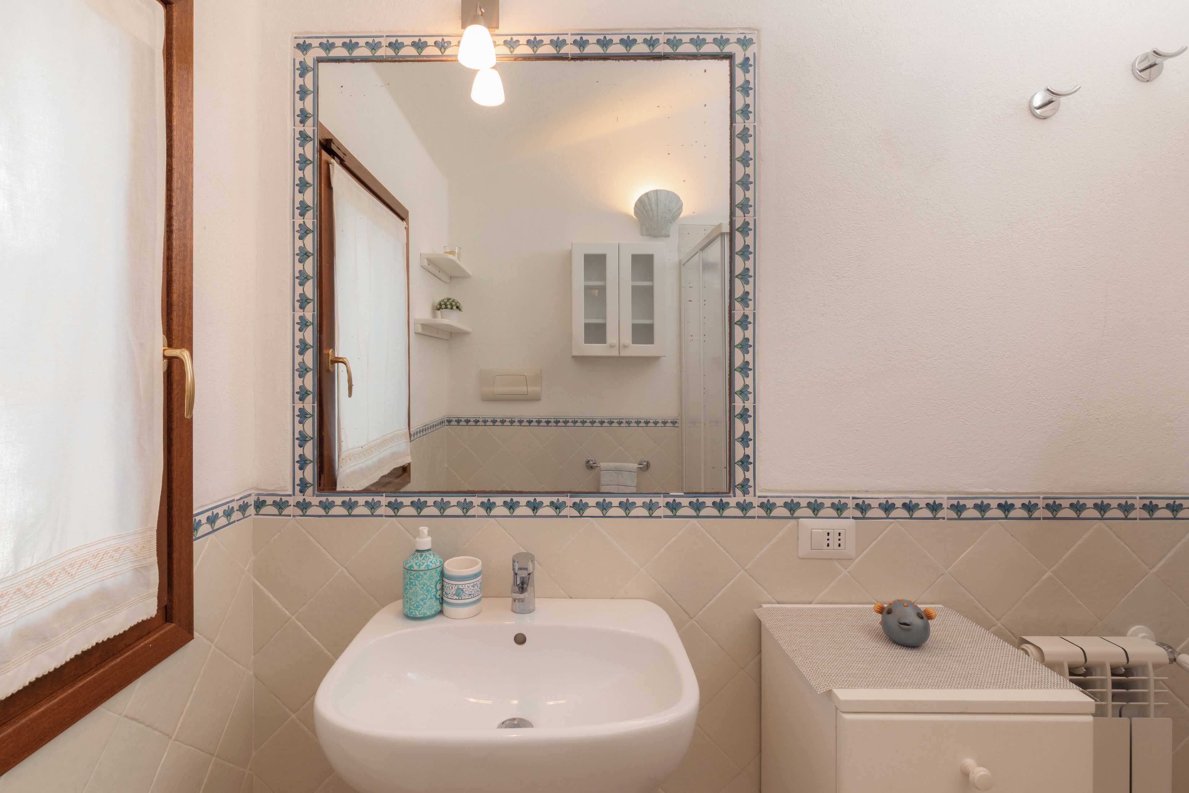 A bathroom with a white sink, a mirror with a decorative border, and a toilet with a towel rack.