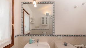 Casa de banho com lavatório branco, espelho com moldura decorativa e sanita com suporte para toalhas.