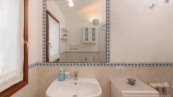 A bathroom with a white sink, a mirror with a decorative border, and a toilet with a towel rack.