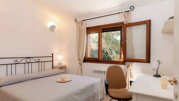 A bedroom with a bed, a desk, a chair, a window with curtains, a lamp, and a radiator.