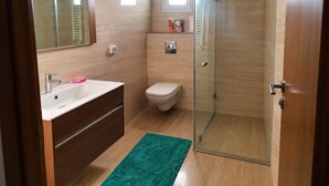 A bathroom with a glass shower enclosure, a toilet, a sink with a mirror, and a green rug. - Elegant High-End Apartment (Tunis Governorate)