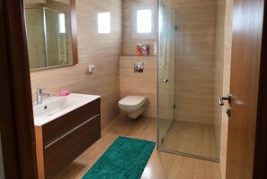 Ein Badezimmer mit Duschkabine aus Glas, Toilette, Waschbecken mit Spiegel und einem grünen Teppich.