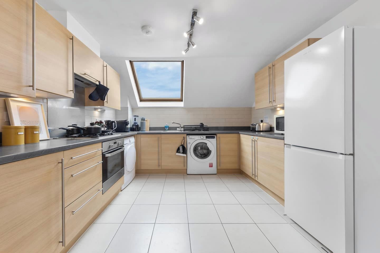 A modern kitchen with a skylight, built-in oven, washing machine, and a refrigerator.