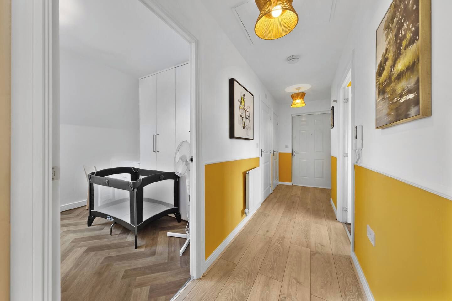 A hallway with a baby playpen, white and yellow walls, and a wooden floor.
