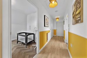 A hallway with a baby playpen, white and yellow walls, and a wooden floor. - Welcome to our  2-bedroom apartment in "Hayes, West London" perfect for up to 4–5 guests. Ideal for families, business travelers, couples and small groups. (Greater London)