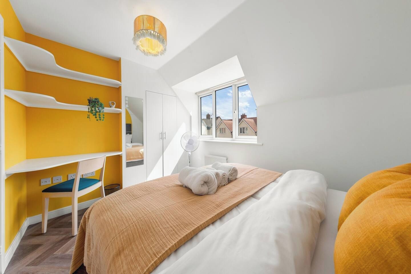 A bedroom with a bunk bed, a desk, and a window with a view of houses.