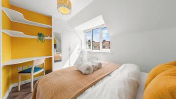 A bedroom with a bunk bed, a desk, and a window with a view of houses.
