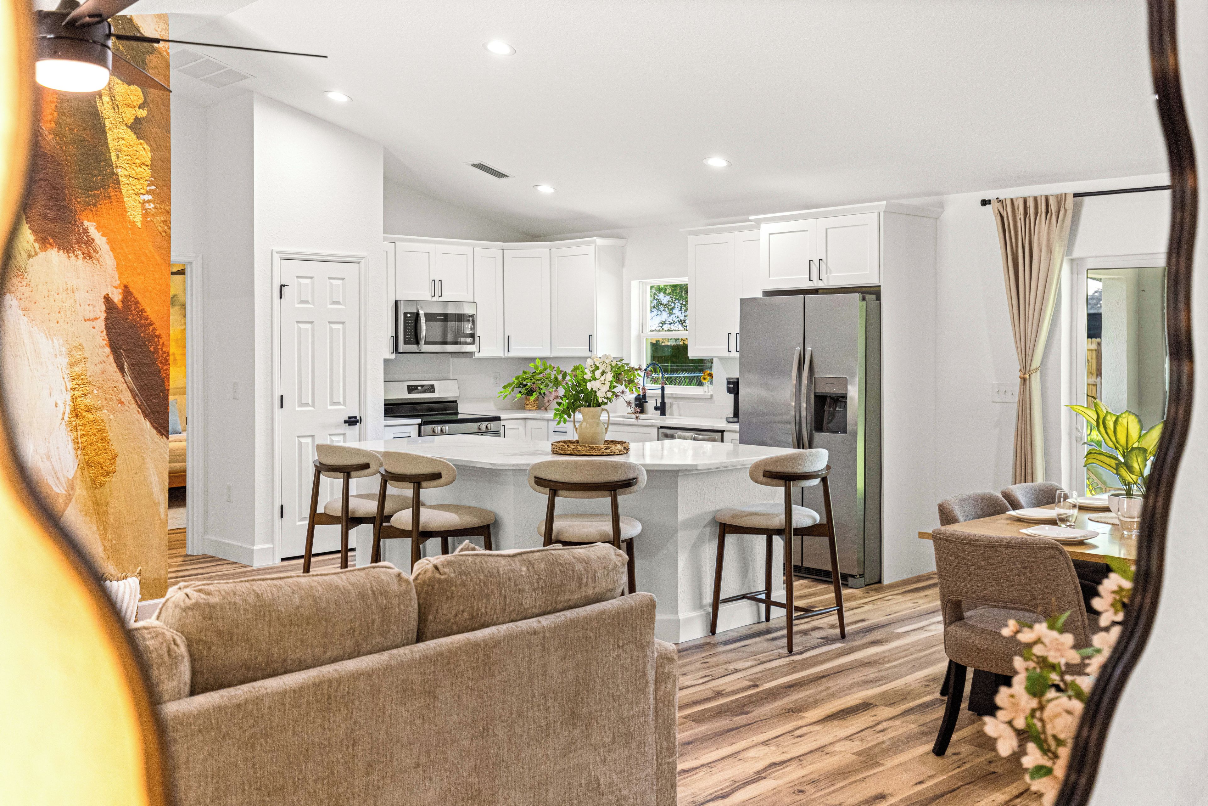 A modern kitchen with white cabinetry, a central island with bar stools, stainless steel appliances, and a view of the outdoors.