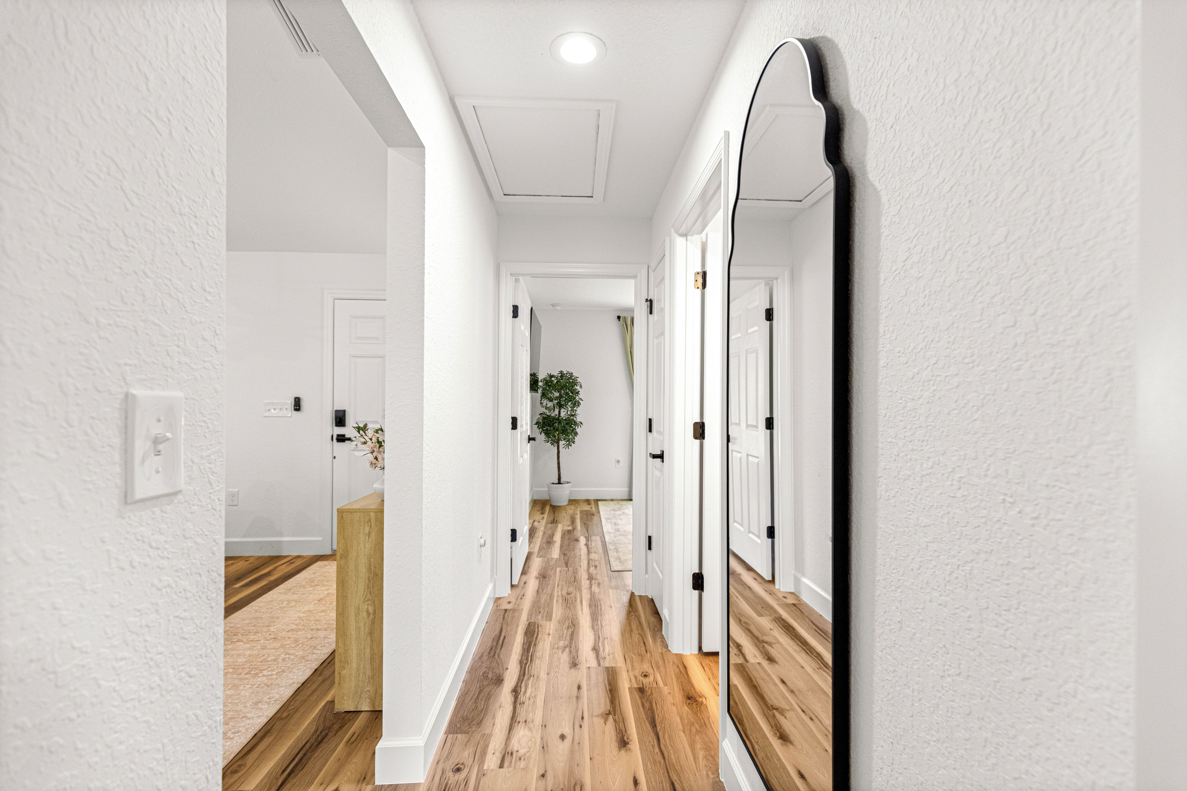 A hallway with white walls, wooden flooring, and a large mirror on the right.