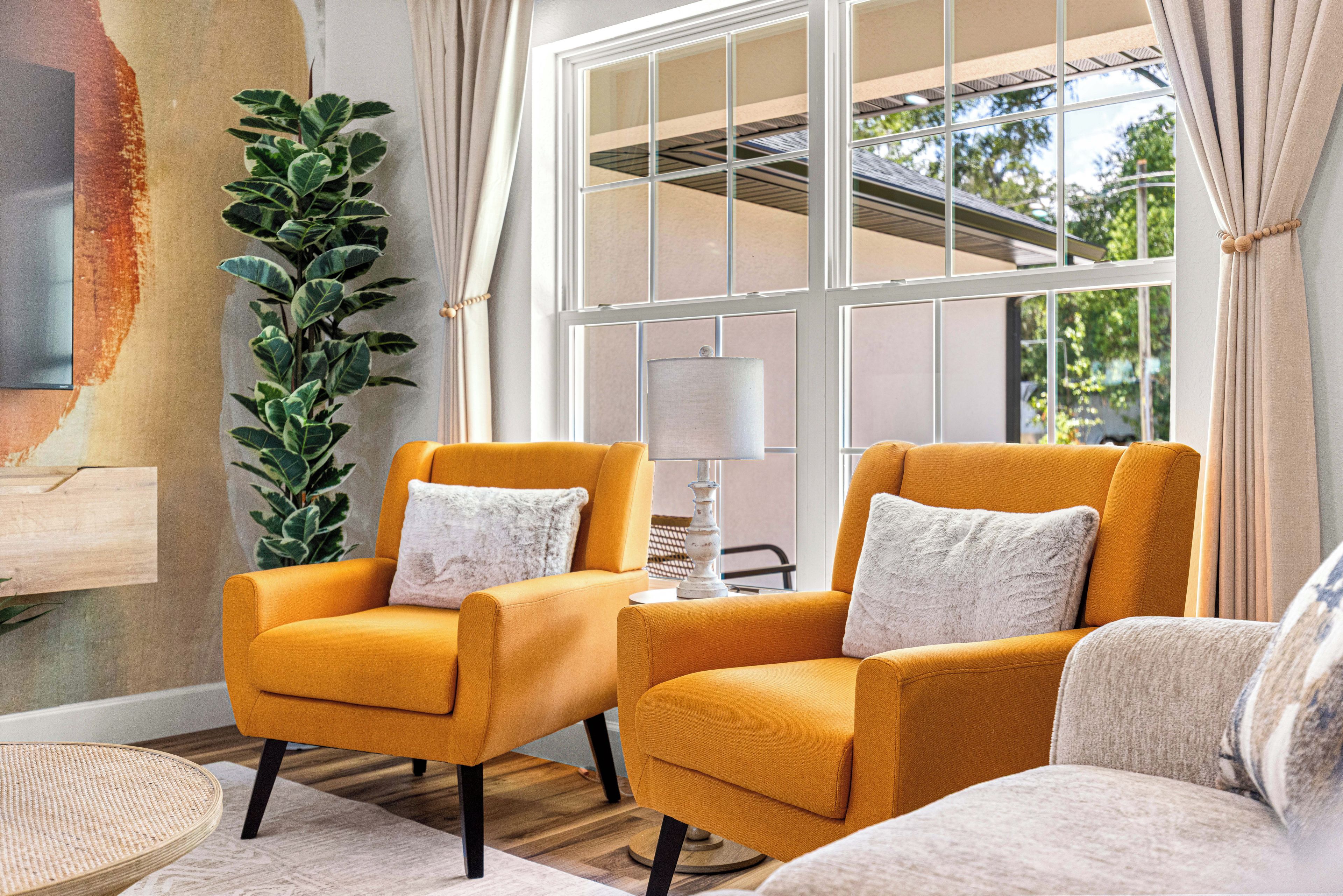 A room with two armchairs, a lamp, a plant, and a large window with curtains.