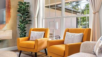 A room with two armchairs, a lamp, a plant, and a large window with curtains.