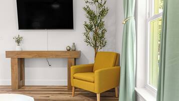 En stue med en gul lænestol, et træbord, et fladskærms-tv og en potteplante.