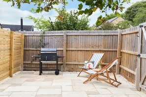 A backyard with a barbecue grill, a folding chair, and a wooden fence.