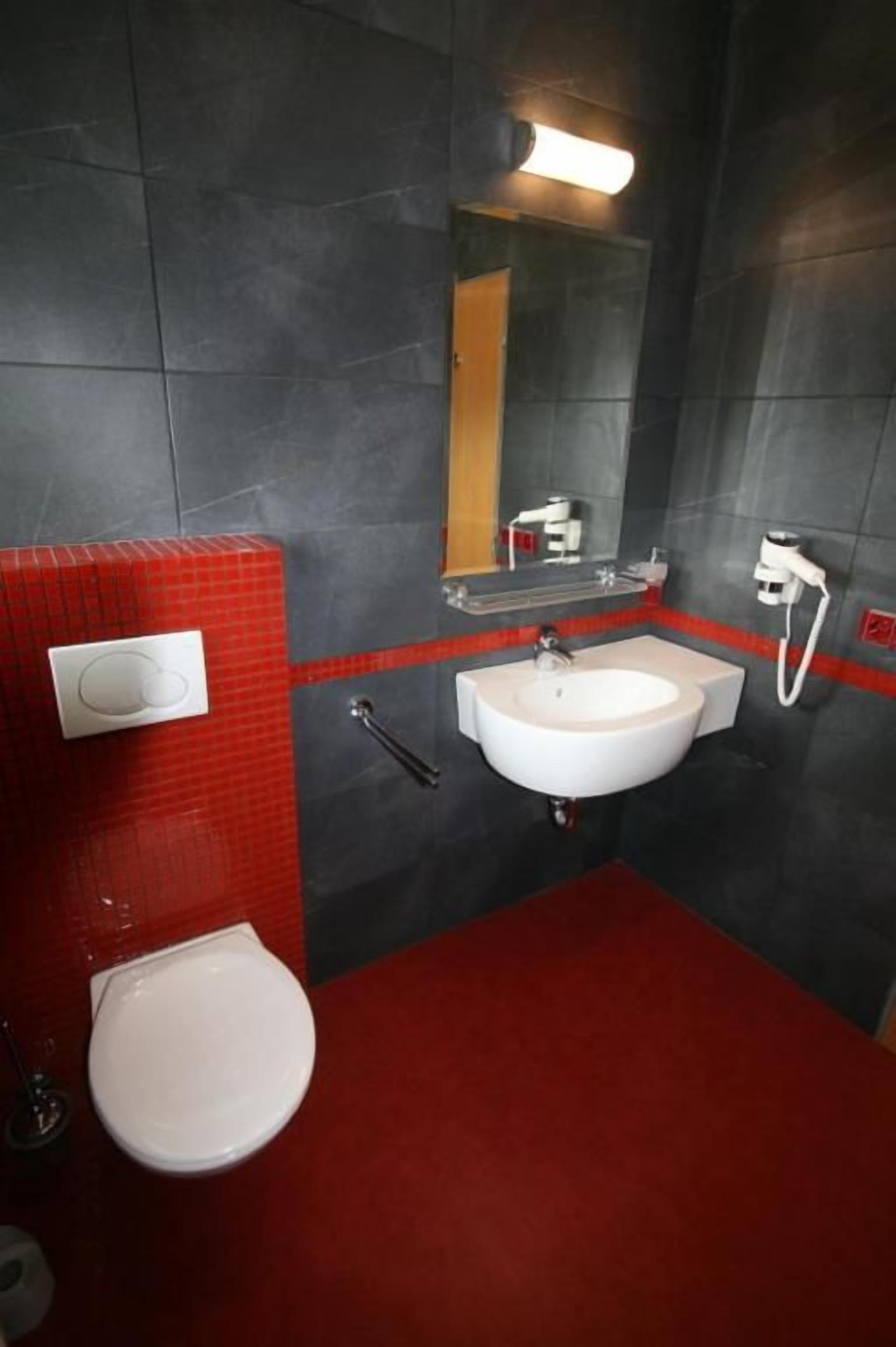 Ein Badezimmer mit rotem Boden, einem weißen Waschbecken und einer Toilette.