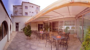 An outdoor patio area with tables and chairs, a covered seating area, and a building in the background.