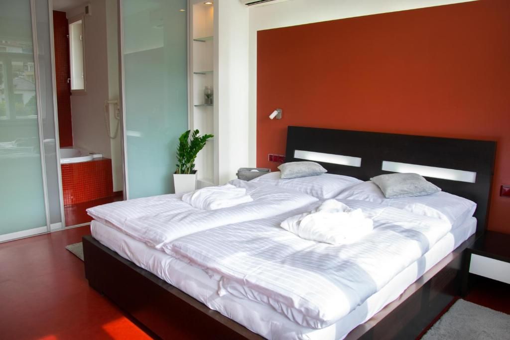 A modern bedroom with a large bed, a red accent wall, and a glass shower enclosure.
