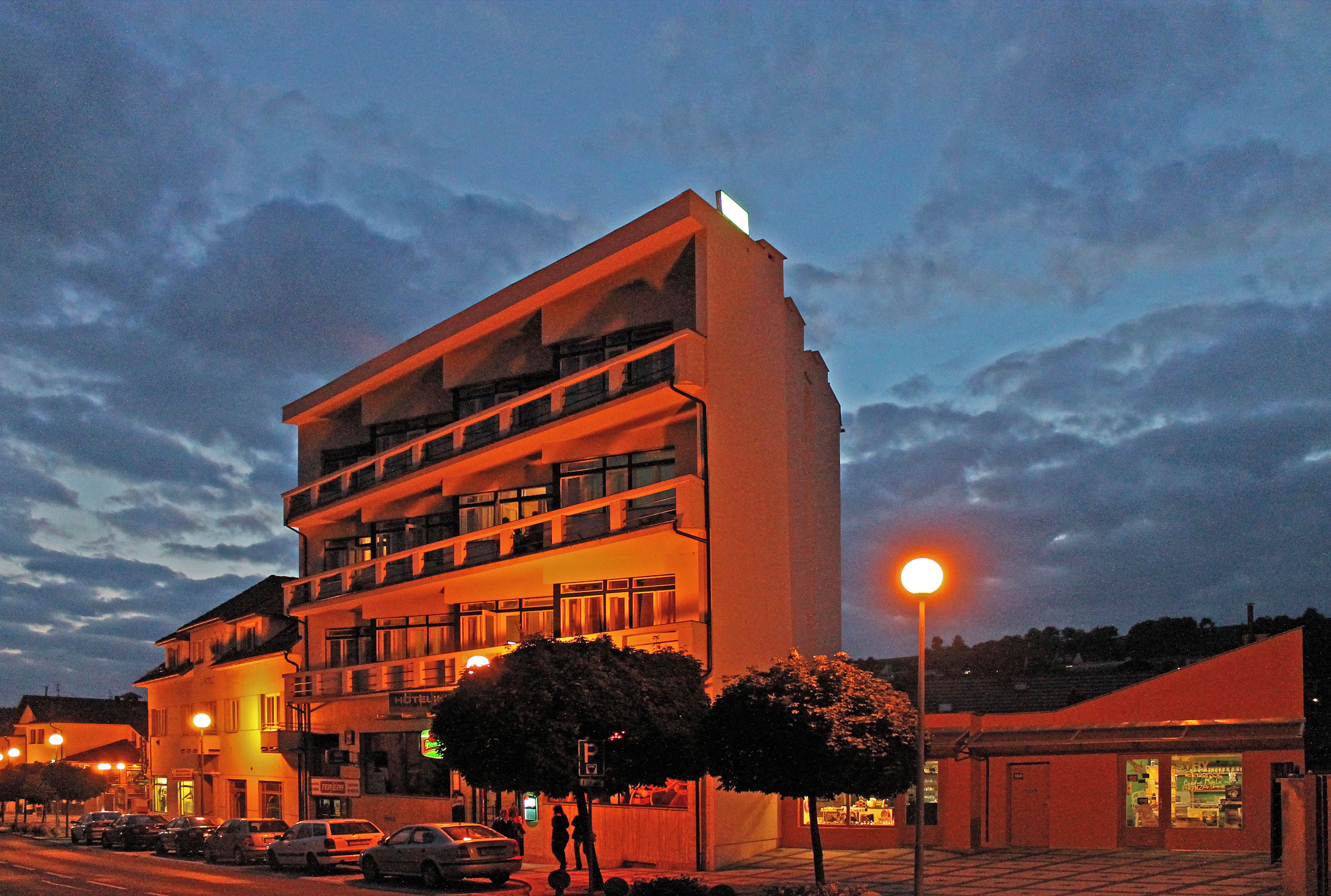 Un hôtel à plusieurs étages doté de balcons, d’un parking et donnant sur la rue, avec une vue particulièrement belle au crépuscule.