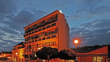 Un hôtel à plusieurs étages doté de balcons, d’un parking et donnant sur la rue, avec une vue particulièrement belle au crépuscule.