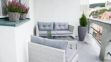 A balcony with wicker furniture, potted plants, and a view of buildings.