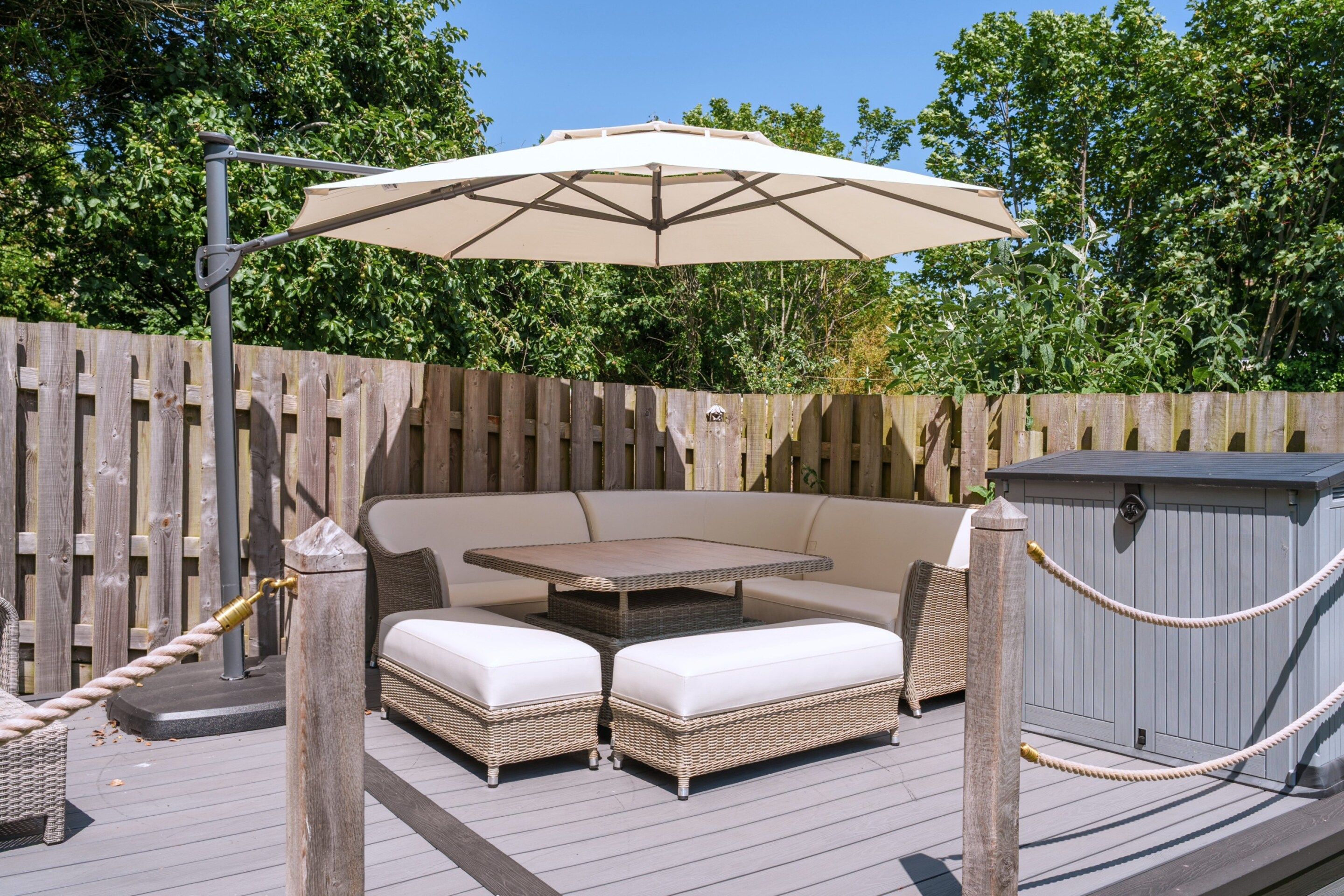 An outdoor patio with a table and two sofas, a wooden deck, a fence, and a storage shed.