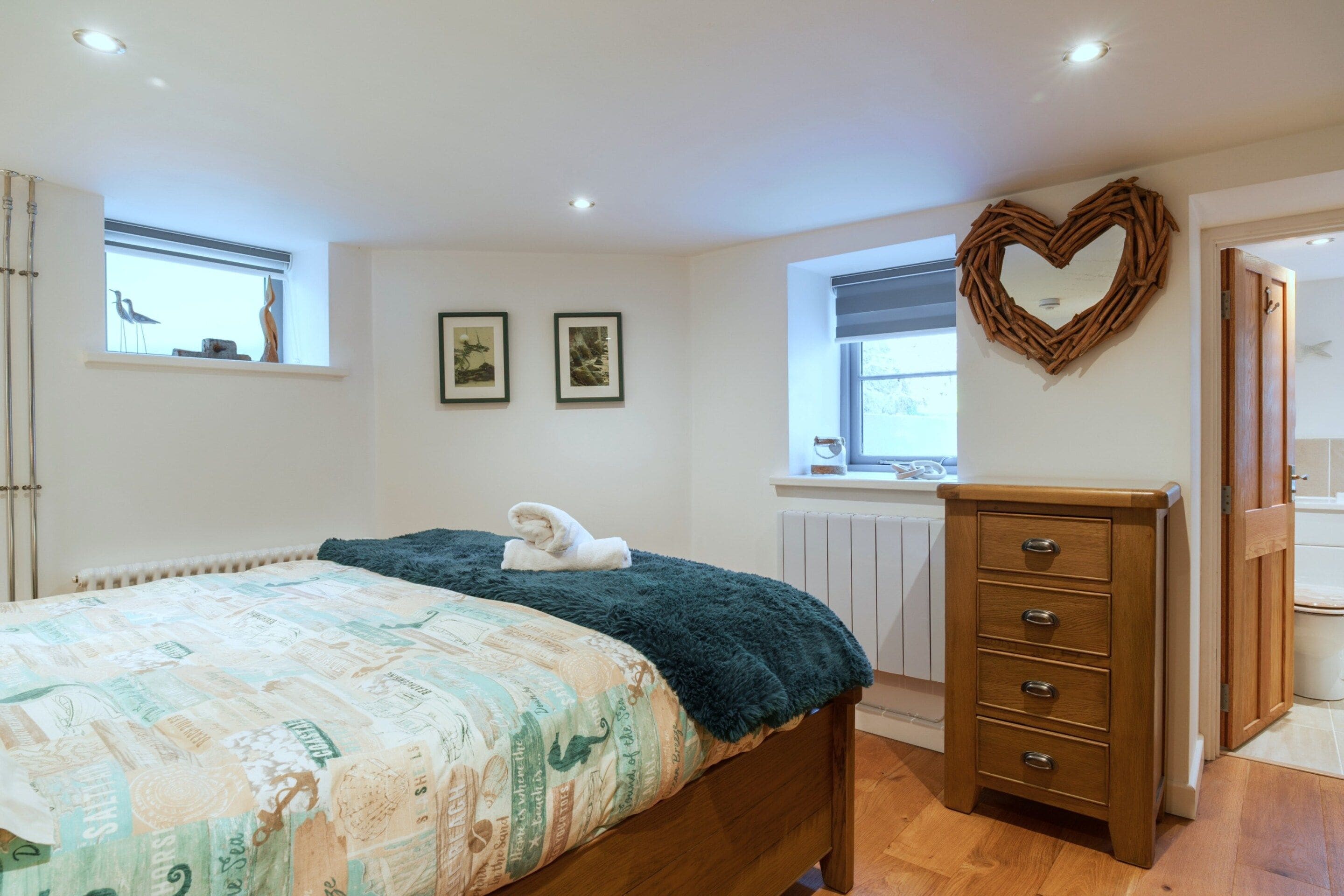 A bedroom with a bed, a dresser, a heart-shaped mirror, and two framed pictures on the wall.
