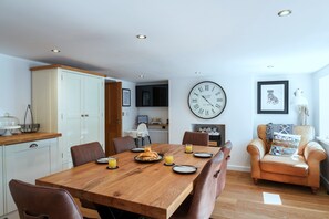 A dining area with a wooden table, chairs, and a large wall clock. - Cawsand Home With Garden (Saltash)