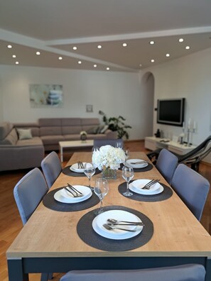 A dining area with a wooden table set for six, surrounded by chairs, with a sofa and a television in the background. - Apartment The Big Chill - Three Bedroom Apartment With Terrace, Balcony and Jacuzzi (Dubrovnik)