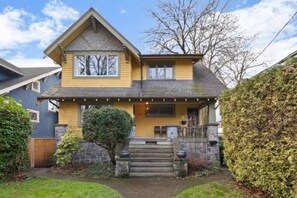 A two-story house with a stone staircase leading to the front door, a small porch with outdoor seating, and a well-maintained garden. - Charming 2BR Kisilano Duplex | Near Jericho Beach (Vancouver)