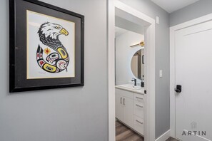 A framed artwork of an eagle on the wall, a bathroom with a mirror and sink, and a door with a lock. - West Van Hideout 2BR Suite | Near Grouse Mountain (West Vancouver)