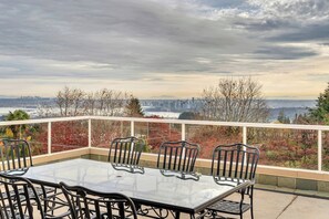 A balcony with a glass table and chairs, overlooking a cityscape and a body of water. - West Vancouver Getaway | Pool & Panoramic Views (West Vancouver)