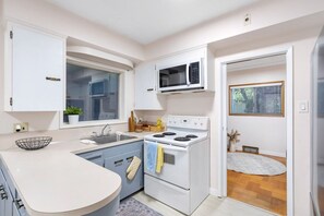 A kitchen with white cabinets, a microwave, a stove, and a sink. - Mid Century Modern Retreat | w/ Indoor Pool (Vancouver)