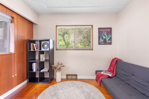 A living room with a dark grey sofa, a black bookshelf, a round grey rug, a window with blinds, and a framed poster on the wall. - Mid Century Modern Retreat | w/ Indoor Pool (Vancouver)