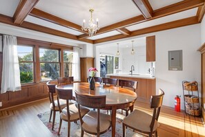 A dining area with a wooden table and chairs, a chandelier, and a view of the kitchen. - Charming 2BR Jericho Home | Private Deck with BBQ! (Vancouver)