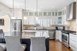 A modern kitchen with white cabinets, stainless steel appliances, and a central island with seating. - Elegant 3BR Family Home - Prime Vancouver Location (Vancouver)