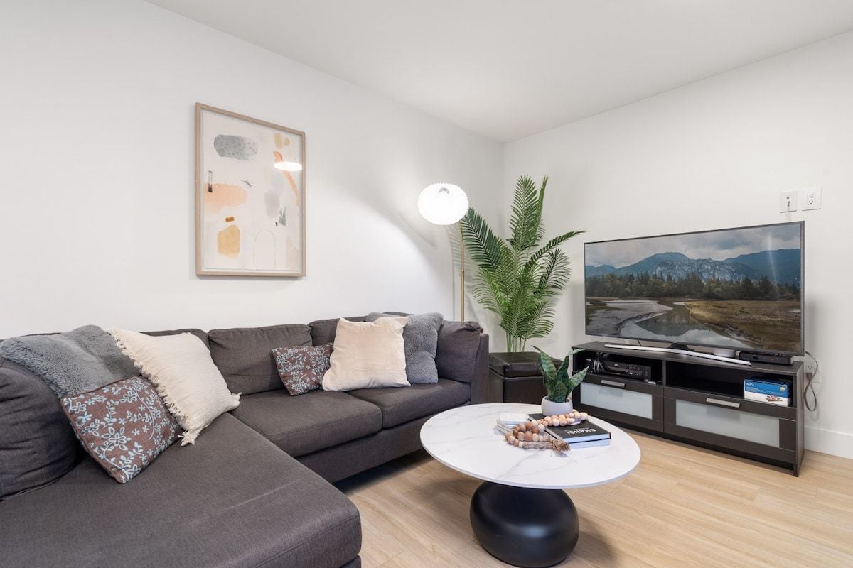 A modern living room with a sectional sofa, a flat-screen TV, a coffee table, and a potted plant.
