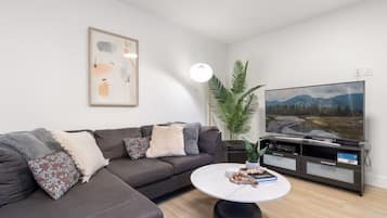 A modern living room with a sectional sofa, a flat-screen TV, a coffee table, and a potted plant.