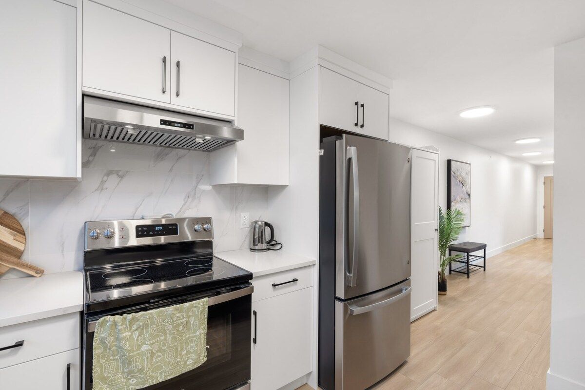 A modern kitchen with stainless steel appliances, white cabinetry, and a marble backsplash.