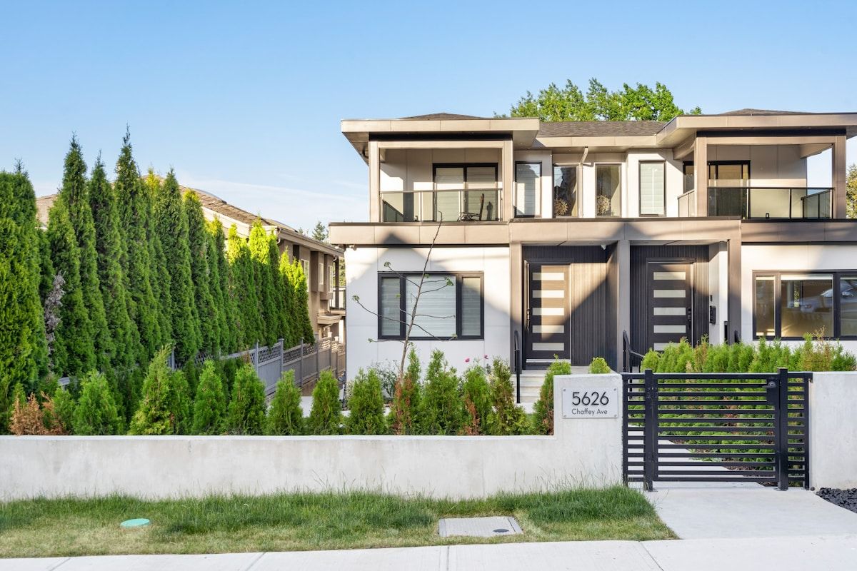 A modern two-story house with a flat roof, large windows, and a black gate.