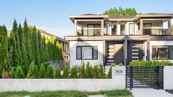 A modern two-story house with a flat roof, large windows, and a black gate.