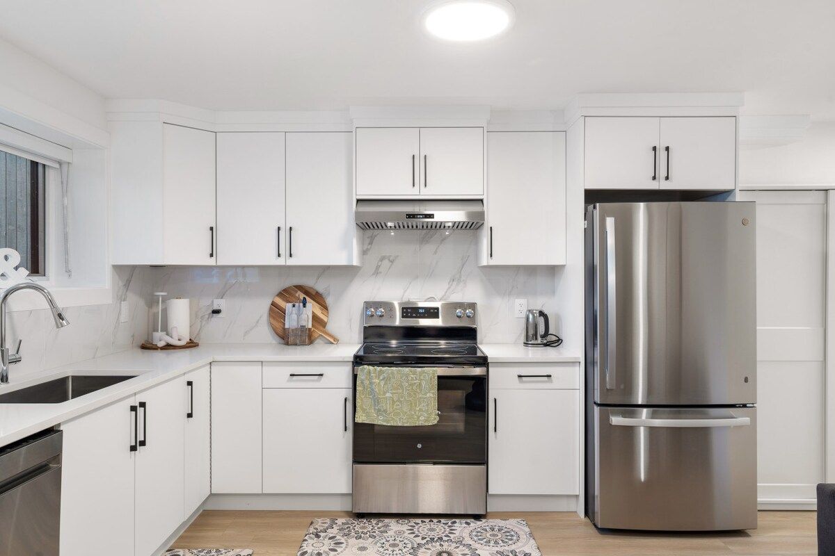 A modern kitchen with white cabinets, stainless steel appliances, and a patterned rug.